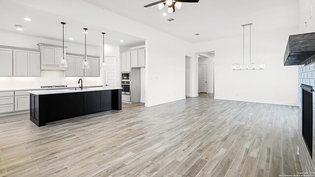 kitchen with a center island with sink, hanging light fixtures, ceiling fan, gas stovetop, and light wood-type flooring