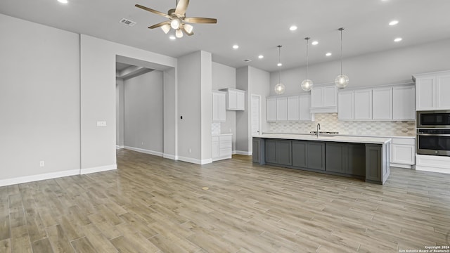 kitchen featuring stainless steel appliances, decorative light fixtures, a kitchen island with sink, white cabinets, and light wood-type flooring