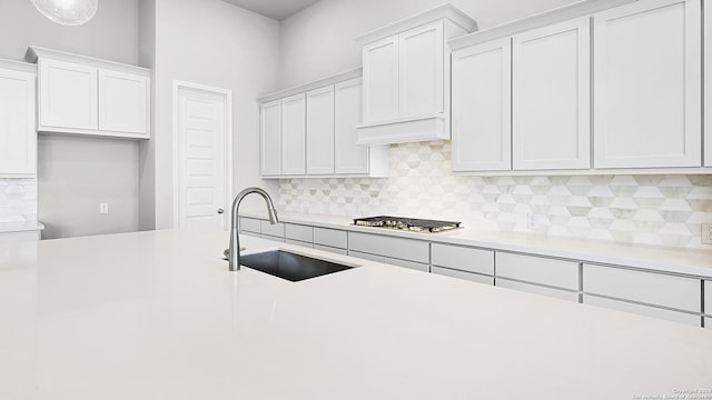 kitchen featuring stainless steel gas stovetop, white cabinetry, sink, and tasteful backsplash