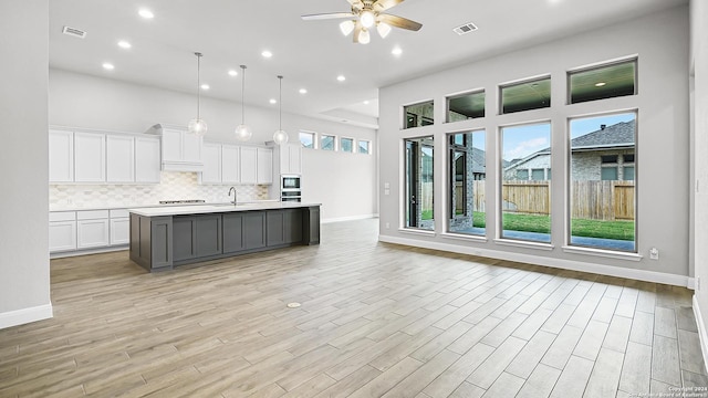 kitchen featuring pendant lighting, light wood-type flooring, white cabinetry, and a kitchen island with sink