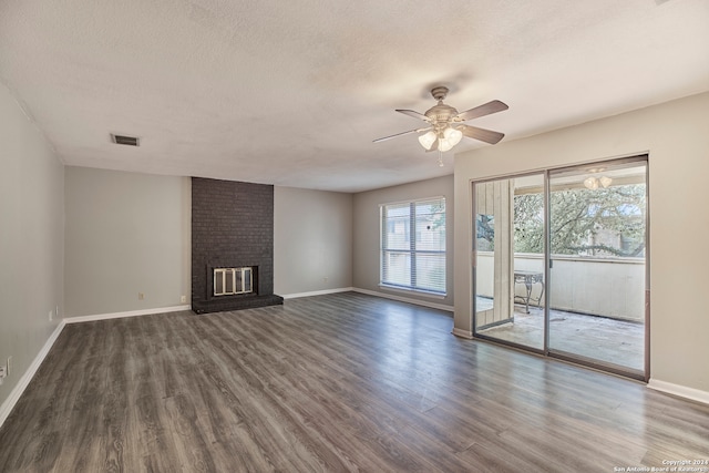 unfurnished living room with ceiling fan, brick wall, a brick fireplace, hardwood / wood-style flooring, and a textured ceiling