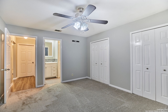 unfurnished bedroom with ceiling fan, light carpet, two closets, and ensuite bath