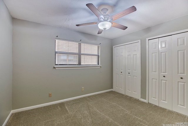 unfurnished bedroom featuring carpet flooring, ceiling fan, and two closets