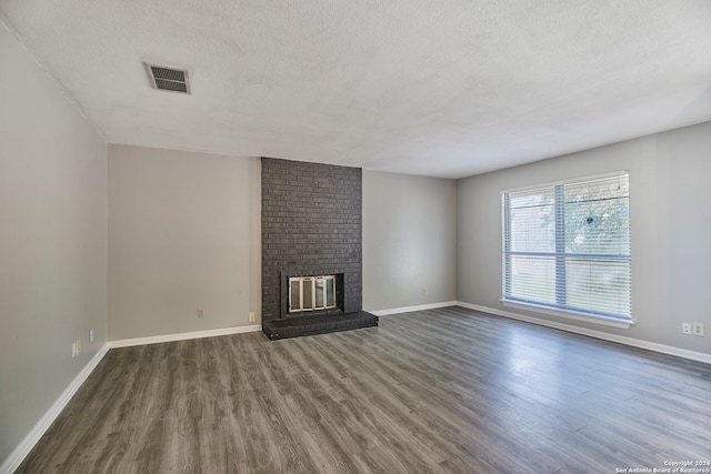 unfurnished living room featuring a textured ceiling, brick wall, hardwood / wood-style flooring, and a brick fireplace