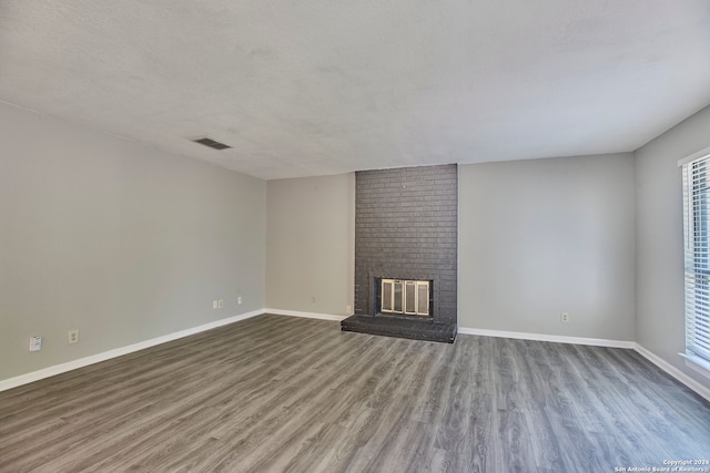 unfurnished living room featuring wood-type flooring, brick wall, a textured ceiling, and a fireplace