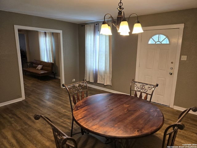 dining area with dark wood-type flooring, a textured wall, a notable chandelier, and baseboards