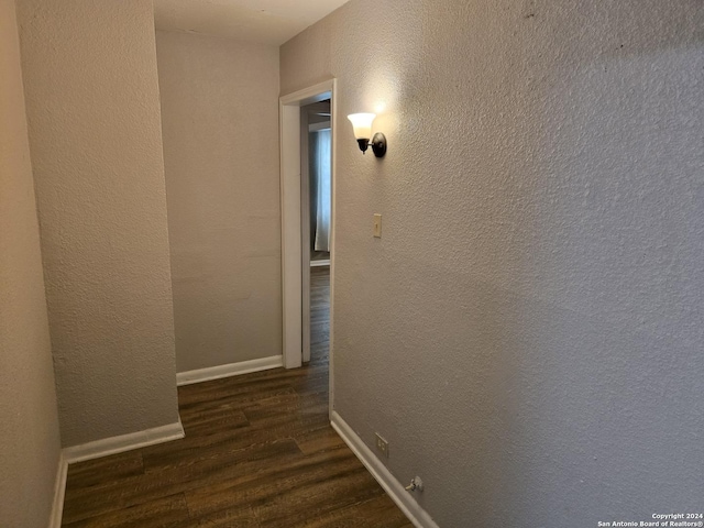 corridor with a textured wall, dark wood finished floors, and baseboards