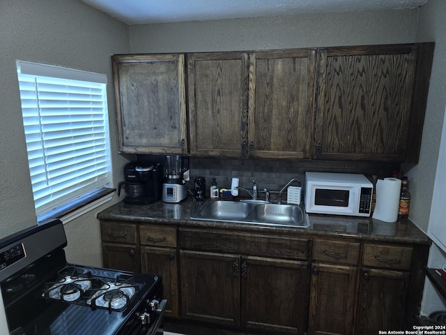 kitchen with a sink, tasteful backsplash, white microwave, dark countertops, and stainless steel gas range oven