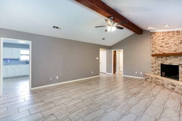 unfurnished living room featuring light tile flooring, a fireplace, ceiling fan, vaulted ceiling with beams, and sink