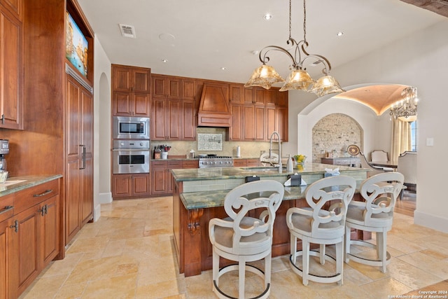 kitchen featuring pendant lighting, sink, an island with sink, appliances with stainless steel finishes, and custom range hood