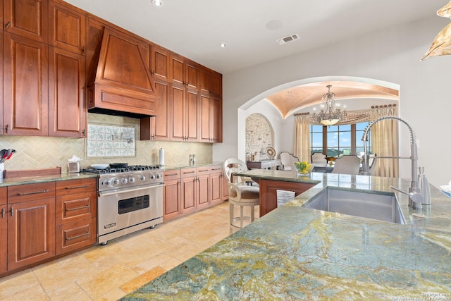 kitchen featuring sink, tasteful backsplash, premium stove, custom range hood, and a chandelier