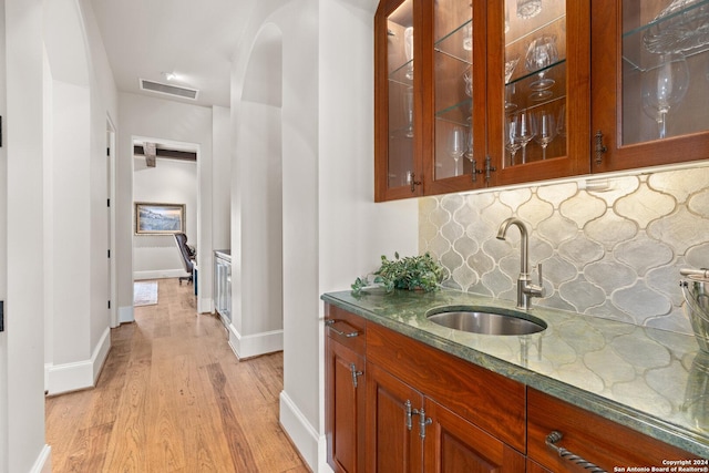 bar featuring light wood-type flooring, backsplash, and sink