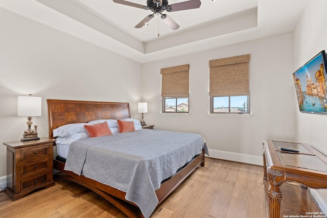 bedroom with ceiling fan, light hardwood / wood-style floors, and a tray ceiling