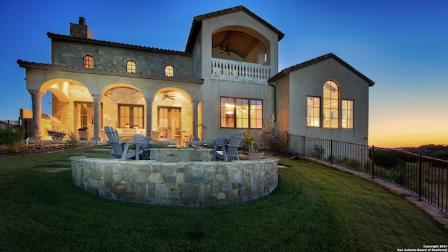 back house at dusk with a yard, a patio, a balcony, and ceiling fan