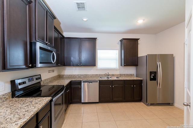 kitchen featuring sink, light stone counters, dark brown cabinets, light tile patterned floors, and appliances with stainless steel finishes