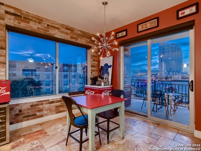 215 Center St Unit 307, San Antonio, TX 78202 - dining room featuring stone tile flooring, a chandelier, brick wall, baseboards, and a view of city