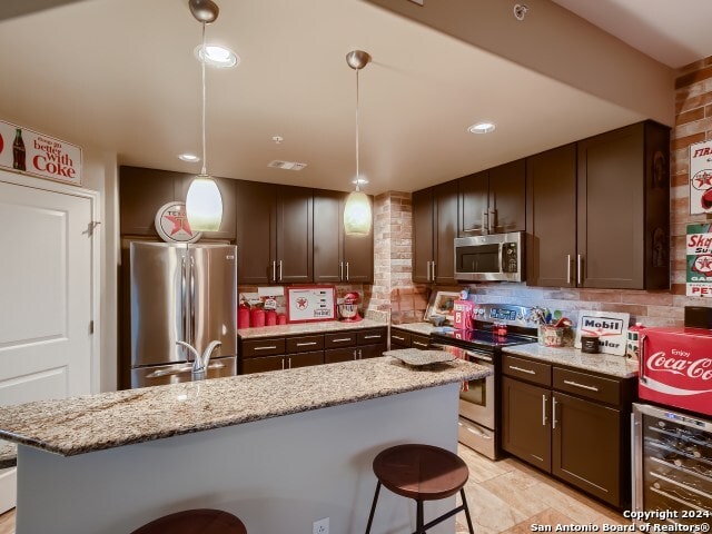 215 Center St Unit 307, San Antonio, TX 78202 - kitchen with wine cooler, stainless steel appliances, a kitchen breakfast bar, decorative backsplash, and dark brown cabinetry
