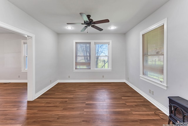 unfurnished room featuring ceiling fan, a healthy amount of sunlight, a wood stove, and dark hardwood / wood-style flooring