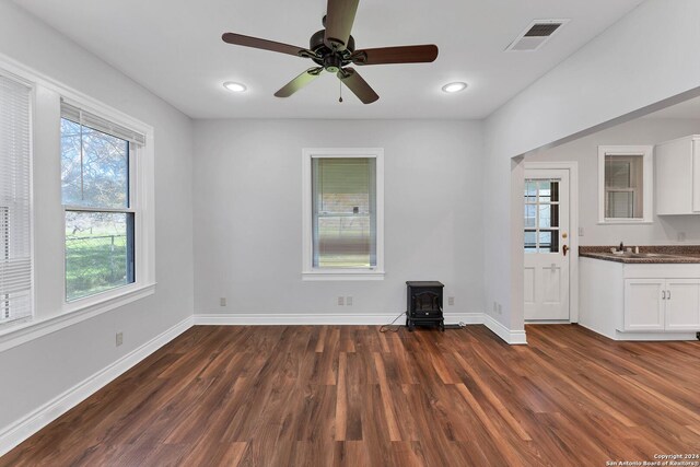 unfurnished living room with a wood stove, dark hardwood / wood-style flooring, and ceiling fan