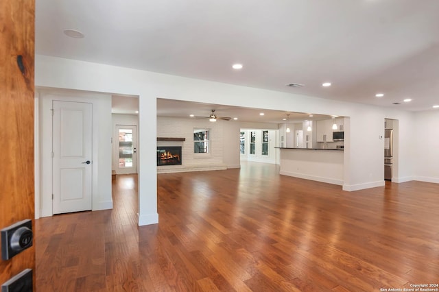 unfurnished living room with ceiling fan, wood-type flooring, and a brick fireplace