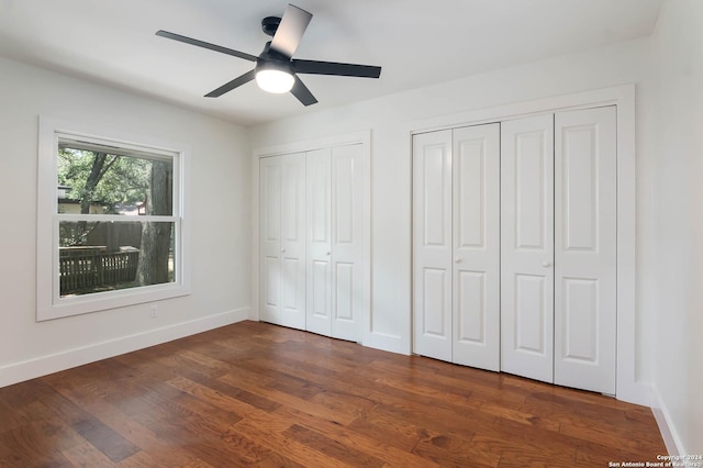 unfurnished bedroom with dark hardwood / wood-style floors, ceiling fan, and multiple closets