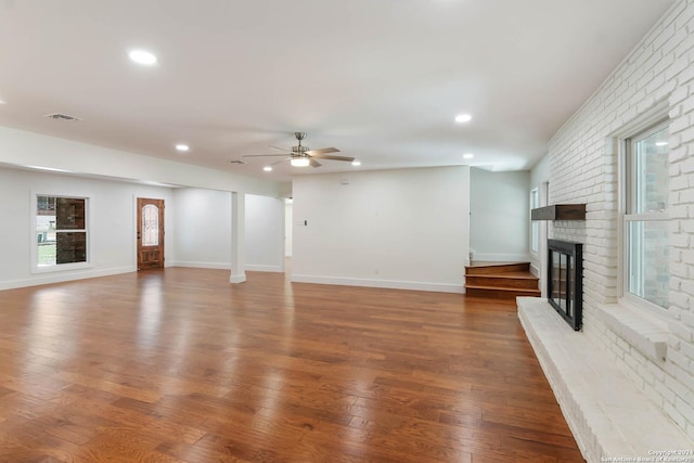 unfurnished living room with ceiling fan, a fireplace, and dark wood-type flooring