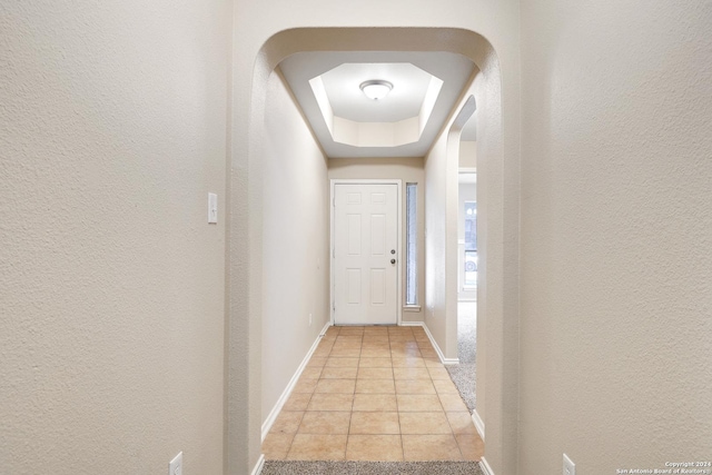 hall with light tile patterned floors and a tray ceiling