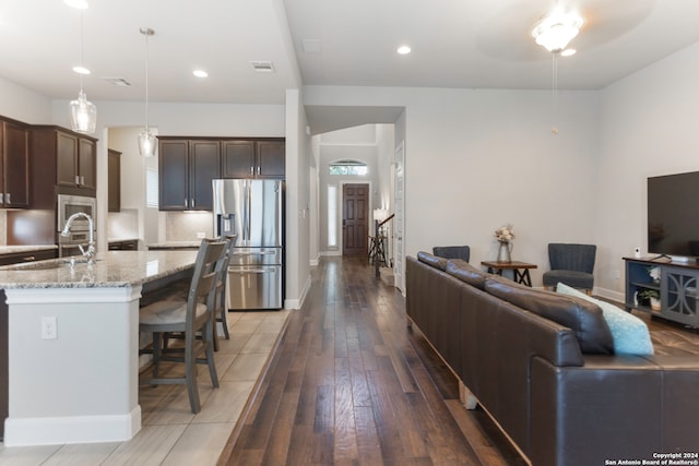 kitchen with dark brown cabinets, stainless steel refrigerator with ice dispenser, pendant lighting, light stone countertops, and a breakfast bar area