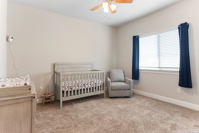 carpeted bedroom with ceiling fan and a crib