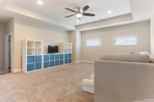 carpeted living room with ceiling fan and a tray ceiling