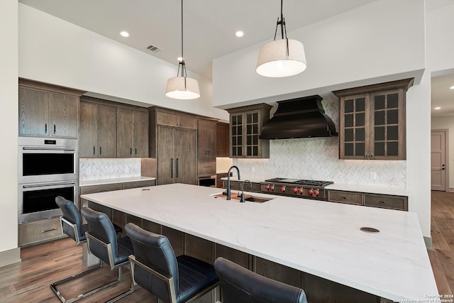 kitchen featuring a large island, sink, stainless steel appliances, premium range hood, and decorative light fixtures