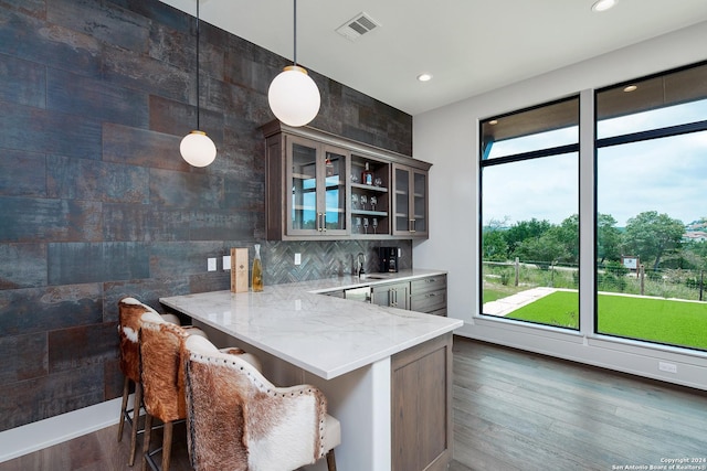 kitchen featuring backsplash, light stone countertops, decorative light fixtures, a kitchen bar, and kitchen peninsula