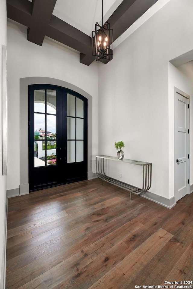 foyer entrance with french doors, an inviting chandelier, dark wood-type flooring, and beam ceiling