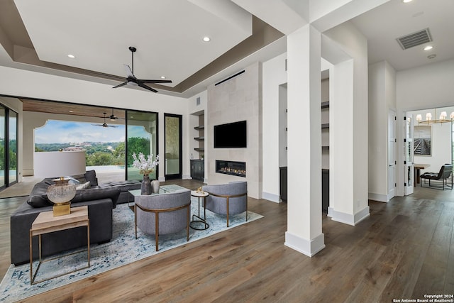 living room featuring built in shelves, a fireplace, ceiling fan with notable chandelier, and dark wood-type flooring