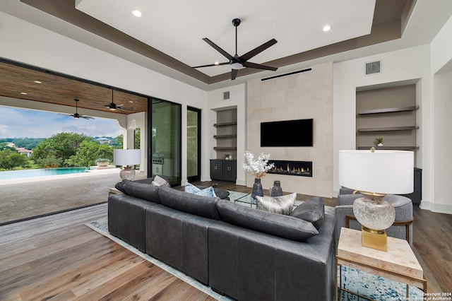 living room with hardwood / wood-style flooring, built in shelves, a raised ceiling, and a tiled fireplace