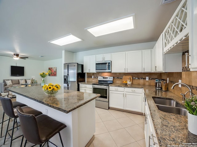 kitchen featuring sink, stainless steel appliances, dark stone countertops, a kitchen bar, and white cabinets