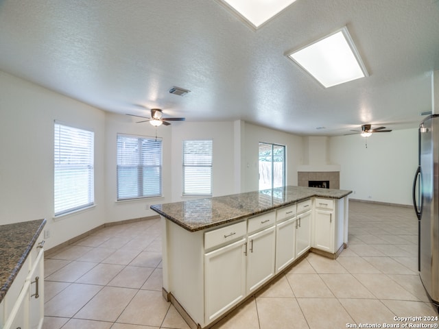 kitchen featuring white cabinets, dark stone countertops, stainless steel fridge, a tiled fireplace, and light tile patterned floors