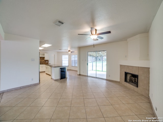 unfurnished living room with ceiling fan, light tile patterned floors, a textured ceiling, and a tiled fireplace