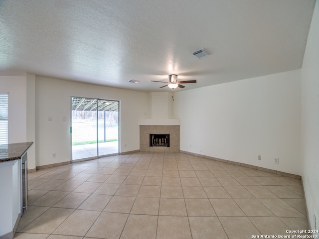 unfurnished living room featuring a tile fireplace, light tile patterned floors, a textured ceiling, and ceiling fan