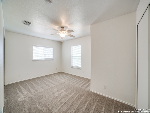 carpeted spare room featuring ceiling fan and a textured ceiling