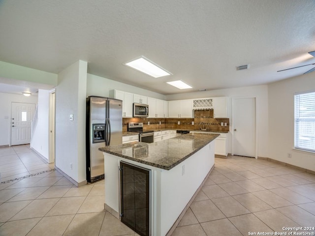 kitchen with dark stone counters, white cabinets, a kitchen island, appliances with stainless steel finishes, and light tile patterned flooring