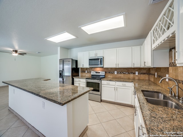 kitchen with appliances with stainless steel finishes, sink, light tile patterned floors, dark stone countertops, and white cabinetry