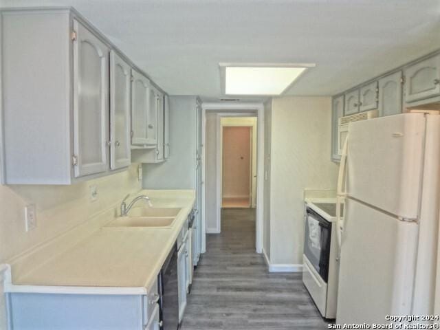 kitchen with white appliances, wood finished floors, baseboards, a sink, and light countertops