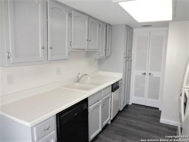 kitchen with a sink, dark wood finished floors, light countertops, dishwashing machine, and dishwasher