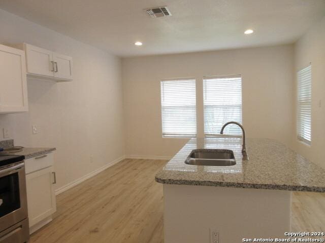 kitchen featuring electric stove, sink, a kitchen island with sink, light stone countertops, and white cabinets