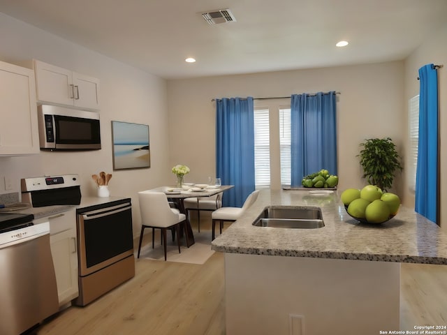 kitchen featuring white cabinetry, stainless steel appliances, a kitchen island with sink, and light wood-type flooring