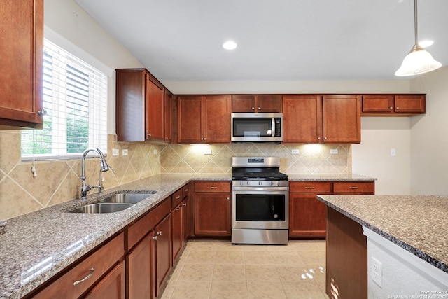 kitchen with sink, light tile patterned floors, light stone countertops, appliances with stainless steel finishes, and decorative light fixtures