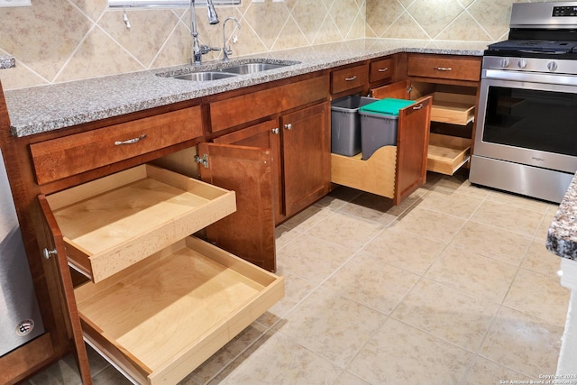 kitchen with light stone counters, sink, stainless steel range, and tasteful backsplash