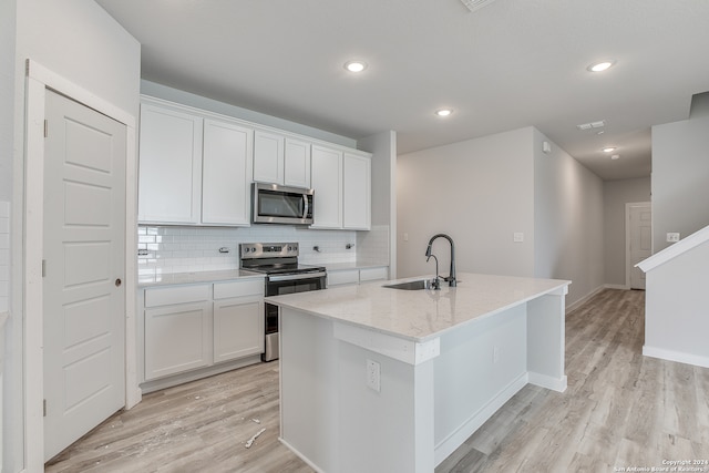 kitchen with light stone countertops, appliances with stainless steel finishes, sink, white cabinets, and an island with sink