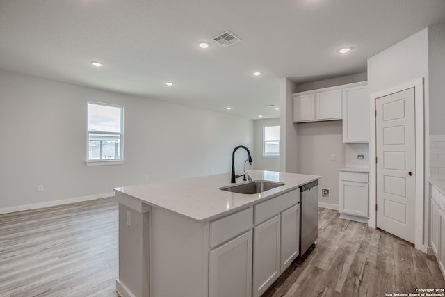 kitchen featuring sink, light hardwood / wood-style flooring, stainless steel dishwasher, an island with sink, and light stone countertops